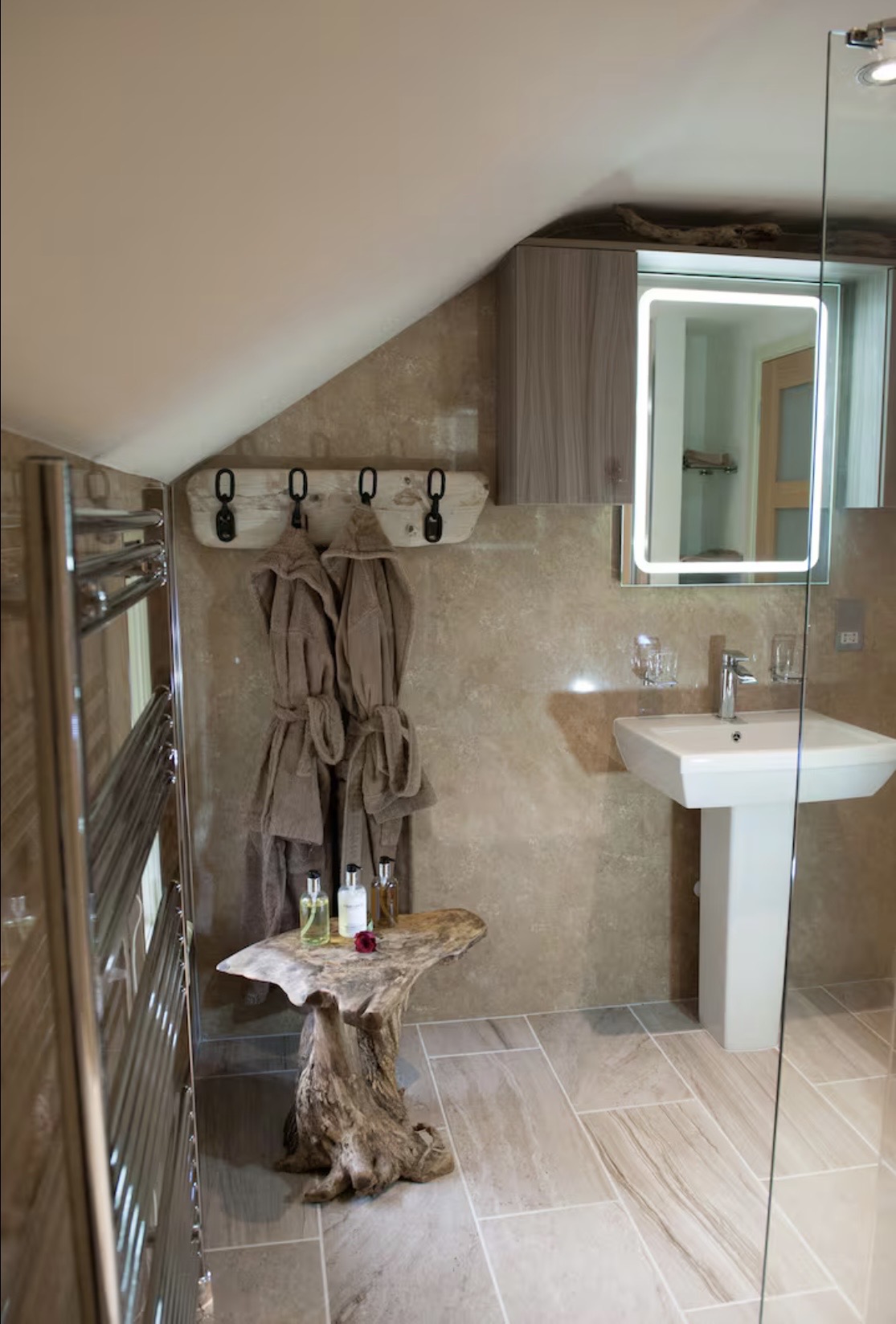 Clean bathroom with bathrobes, heated towel rail, and rustic driftwood details